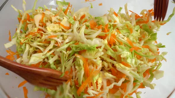 Preparing salad in a glass bowl. Mixing chopped cabbage and carrots.