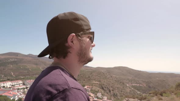 Man with baseball hat and sunglasses walking around hills on sunny summer day