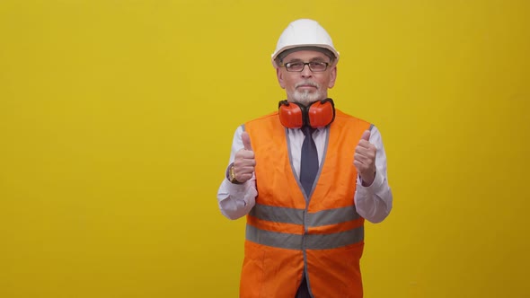 Adult engineer man in uniform shows a thumbs up in the studio, orange background.