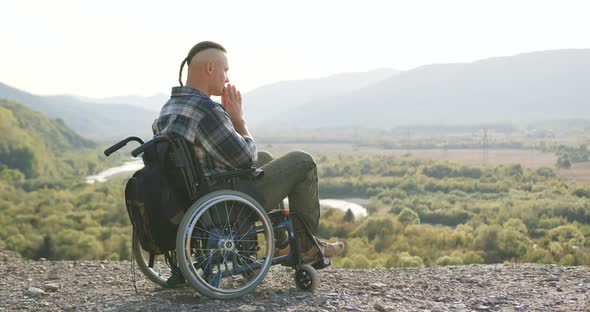 Handsome Calm Concentrated Man with Little Ponytail which Sitting in Wheelchair on the Hill