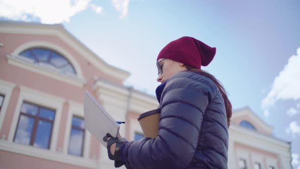 Woman in Red Hat Draws Holds Coffee Cup Sunny Building in the Background