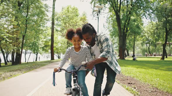 Close Up Portrait of Father Teaches His Daughter to Ride a Twowheeled Bike