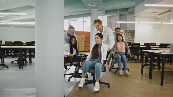 Team of Diverse Joyful Colleagues are Celebrating Success Riding Chairs in Office Laughing and