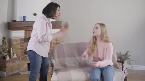 Adult Caucasian Woman and Her Teen Daughter Arguing Indoors. Blond Girl and Mother Yelling at Each