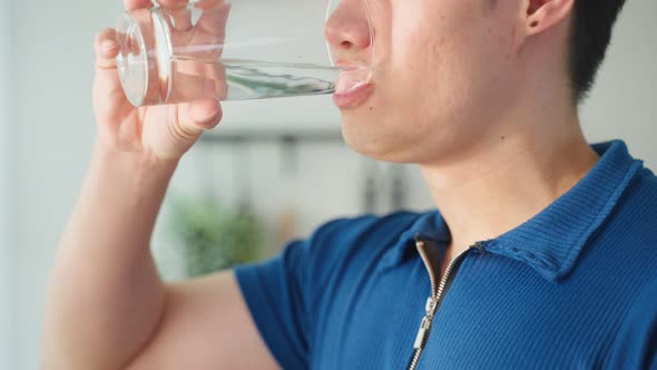 Close up of Asian active strong man drinking clean water after wake up for health in kitchen at home