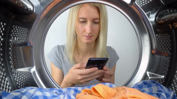 Woman sits in front of washing machine and looks at her smartphone. Instructions