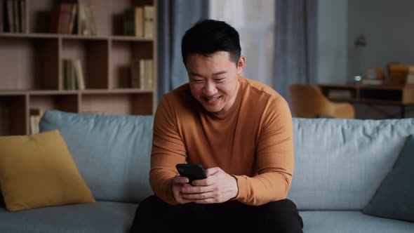 Positive Mature Asian Man Web Surfing on Smartphone Enjoying Content Relaxing at Home Slow Motion