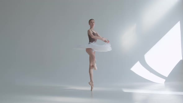 Young Graceful Ballerina in Pointe Shoes and White Ballet Tutu Makes Pirouette, Shot on a White