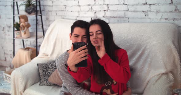 Young Couple Using Smart Phone Talking To Family Congratulates Merry Christmas By Video Call