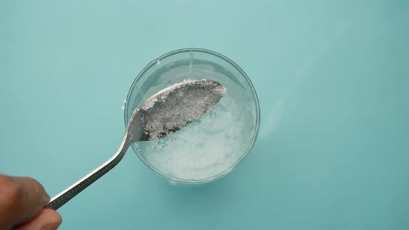 Pouring White Sugar in a Glass of Water on Table