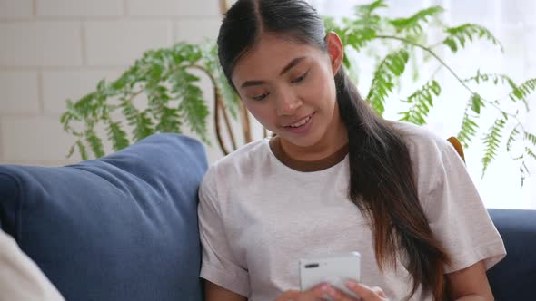 Smile Asian woman sitting on the sofa and using smartphone in the living room.