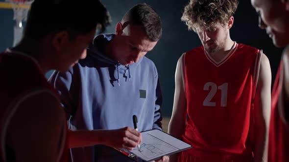 International Basketball Game the Coach Instructs Team Players on the Tactics of Game Using a Tablet