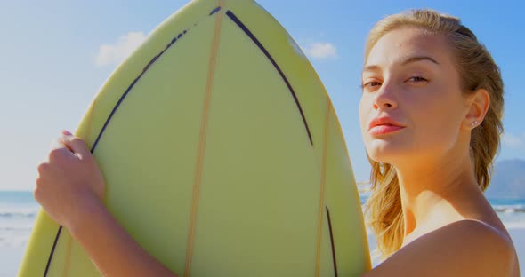 Side view of young Caucasian woman standing with surfboard on the beach 4k