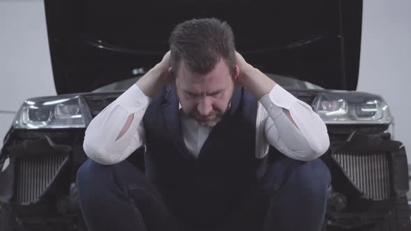 Close-up of Sad Caucasian Businessman in Elegant Clothes Sitting in Front of Broken Car Adult Man