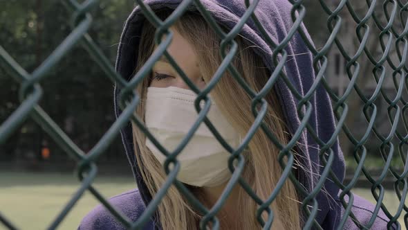 Closed Border. Quarantine. Close-up of Young Woman Wearing Protective Face Mask Stand Behind Fence