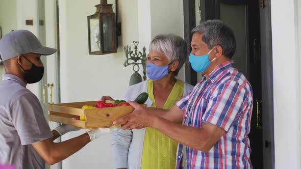 Senior mixed race couple and food delivery man at door wearing face masks