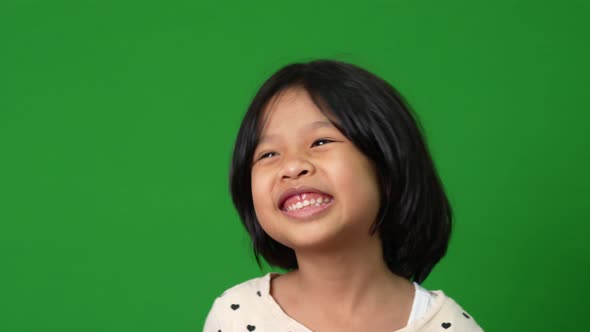 Portrait of happy, smiling, and funny Asian child girl on green screen background, a child looking a