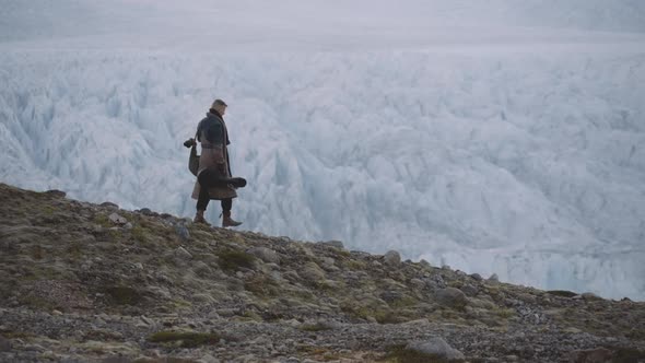 Man With Guitar Case And Greatcoat Walking Along Ridge By Glacier