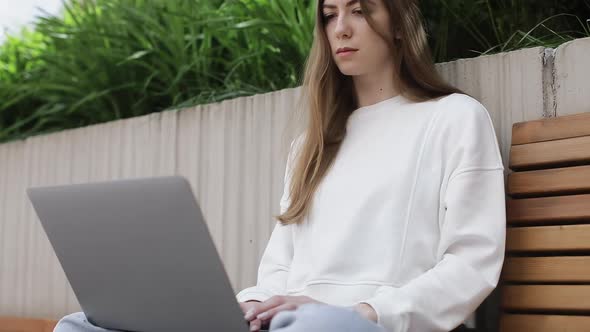 Young Female in Garden Using Laptop Communicates on Internet with Customer