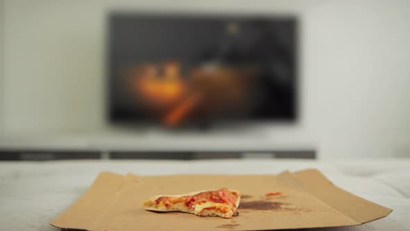 Man Throws a Piece of Halfeaten Pizza on the Sofa in Front of the TV