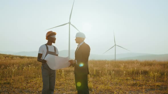 Two Multiracial Industrial Workers Examining Wind Turbines Blueprints with
