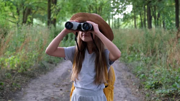 Little Girl Tourist in Hat with Backpack Looking Through Binoculars in the Forest with a Surprised
