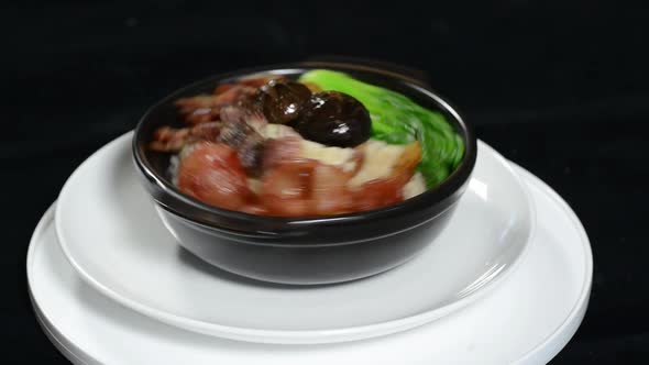 A Person Spinning A Bowl With Cooked Meat And Vegetables Over A Small Plate - Closeup Shot