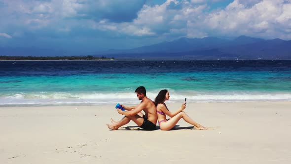 Family of two sunbathing on tropical seashore beach wildlife by blue green ocean with white sandy ba