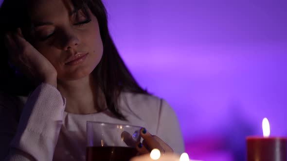 Pretty Woman Is Drinking Warm Tea at Home Sitting in Dark Room with Romantic Candlelight Closeup