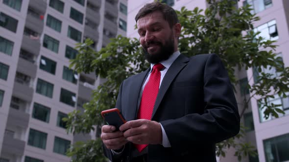 A Serious Middleaged Businessman in Luxurious Clothes in the Financial District of a Metropolis Uses