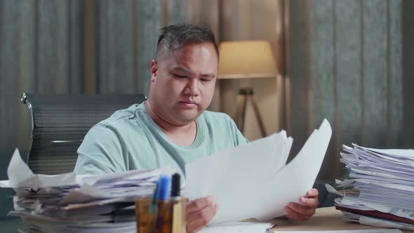 Close Up Of Fat Asian Man Stretching While Working Hard With Documents At The Office