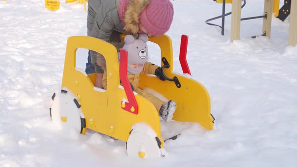 Mom puts her newborn daughter 12-23 months on a wooden spring-loaded car