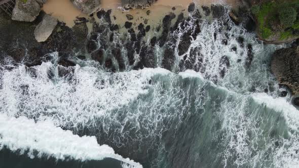 Top down aerial view of giant ocean waves crashing and foaming in coral beach