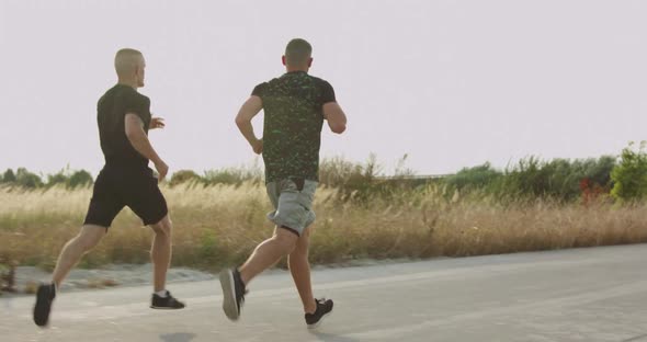 Back View of Two Sportsmen Jogging on a Path Synchronously at Nature on Sunset