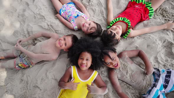 4K Group of Diversity children lying on the beach playing sand together on summer vacation.