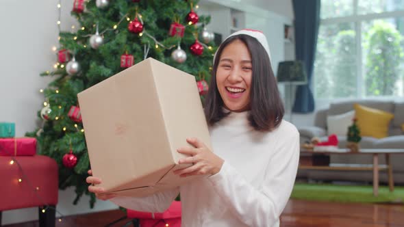 Female teen wear sweater and Christmas hat relax happy hold gift smiling near Christmas tree.