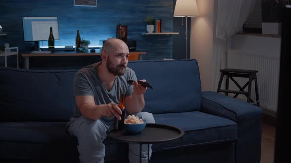 Bored Man Changing Tv Channels Sitting on Cozy Couch Drinking Beer