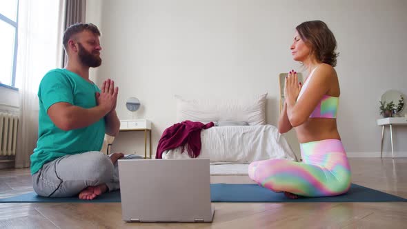 Couple Meditating at Home in Bedroom with Online Yoga Tutorial