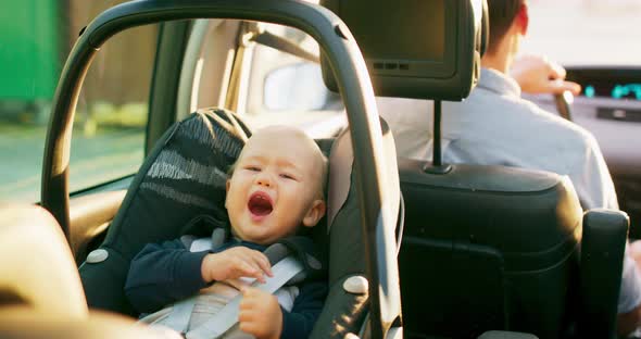 Closeup Laughing Baby Boy Sitting in the Baby Car Seat on the Rear Seat Inside of Car While Car is