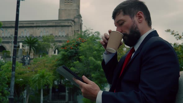 Man Elegant Bearded Working on the Tablet Sitting in the Park on the Bench