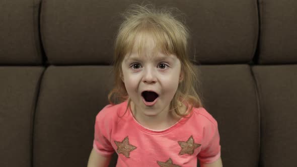 Positive Girl Emotionally Make Faces and Smile in Pink Blouse on Sofa at Home