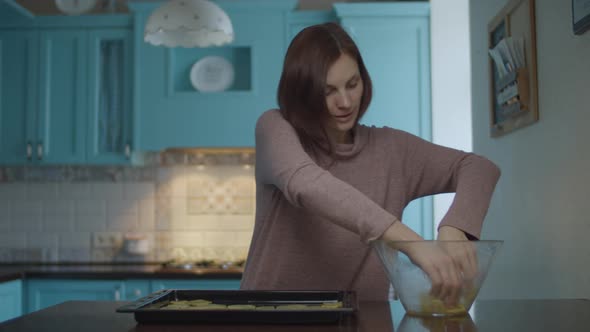 Young Woman Laying Out Potato Slices on Dripping Pan While Cooking Potato Chips at Home. Female