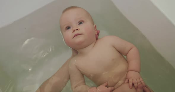 View of Calm Baby Lying on Mom's Hands in Bathroom and Smiling During Swimming