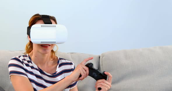 Woman playing joystick game with virtual reality headset on sofa