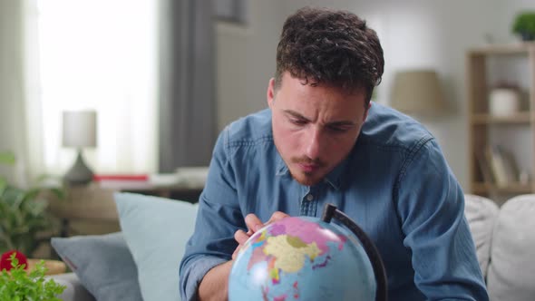 Young Man Looking for Country on Globe at Home in Living Room