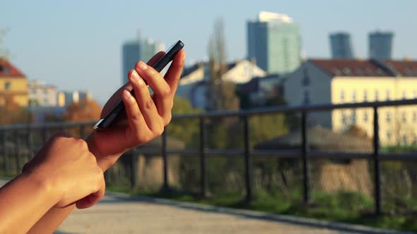 Young Black Woman Works on Smartphone - Buildings in the Background - Closeup