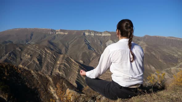 Young Woman Meditating in the Mountains on a Clear Day Back View