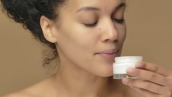 Beauty Portrait of Young African American Woman Twisting Off Jar of Cream and Dissatisfied with Its