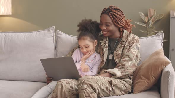 Military Woman and Little Girl Using Laptop Together on Sofa alt