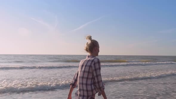 A slender woman walking on the waves of sea water on a sandy beach.